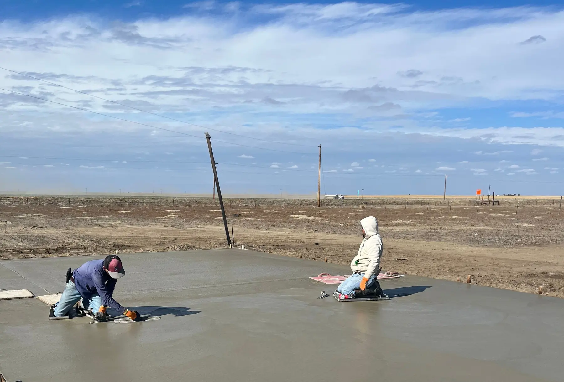 Two finishers working a fresh concrete slab under a big sky on the Colorado plains