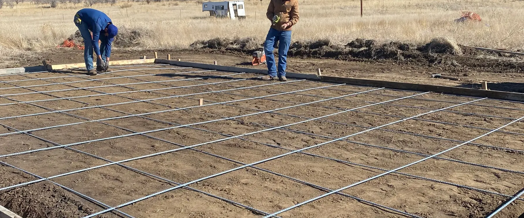 Two crew members setting rebar for a slab on the open plains