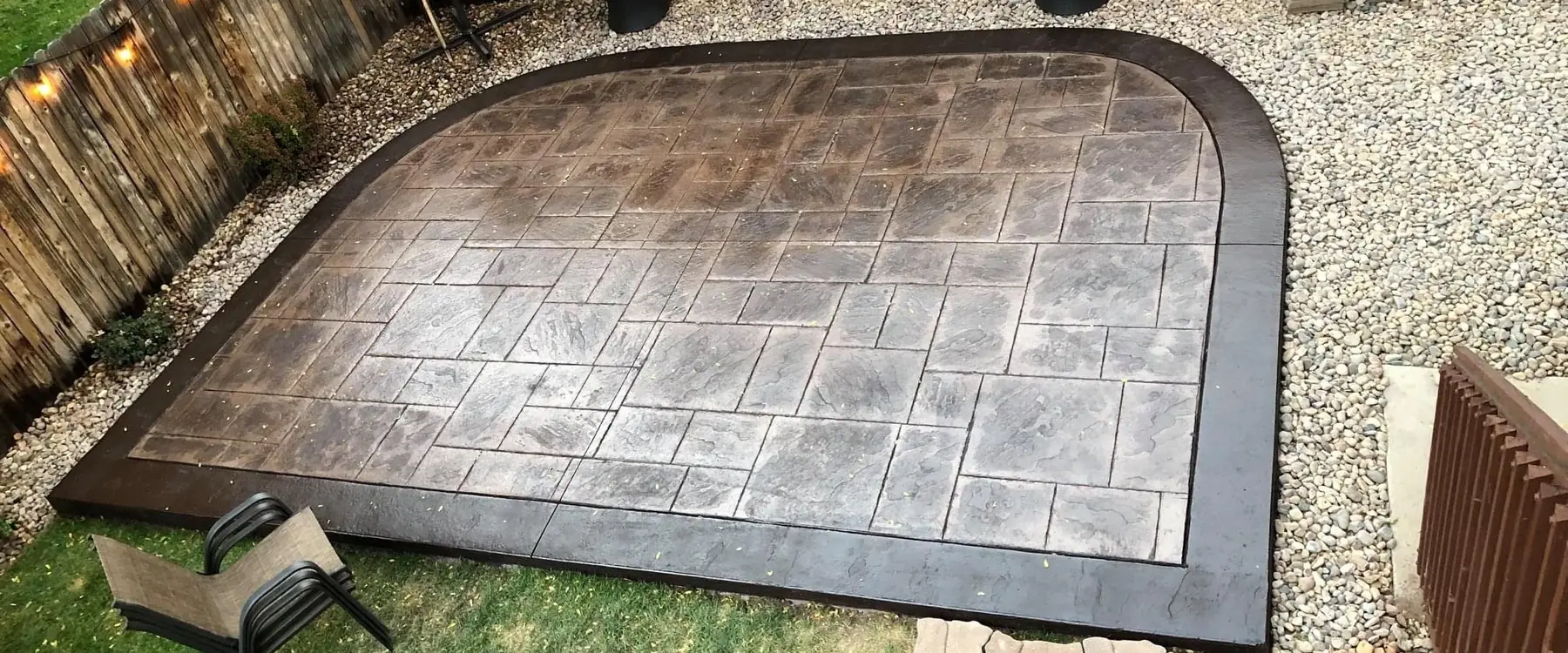 Ashlar-stamped concrete patio with a dark border in a fenced backyard